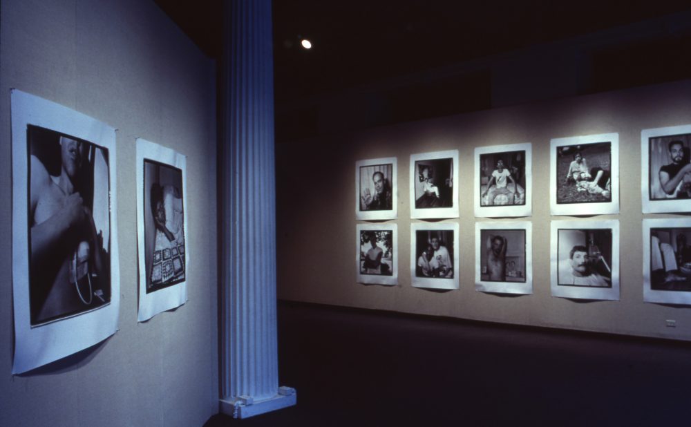Art gallery exhibition with black-and-white photographs on beige walls, divided by a white column. Alt-text generated by AI.