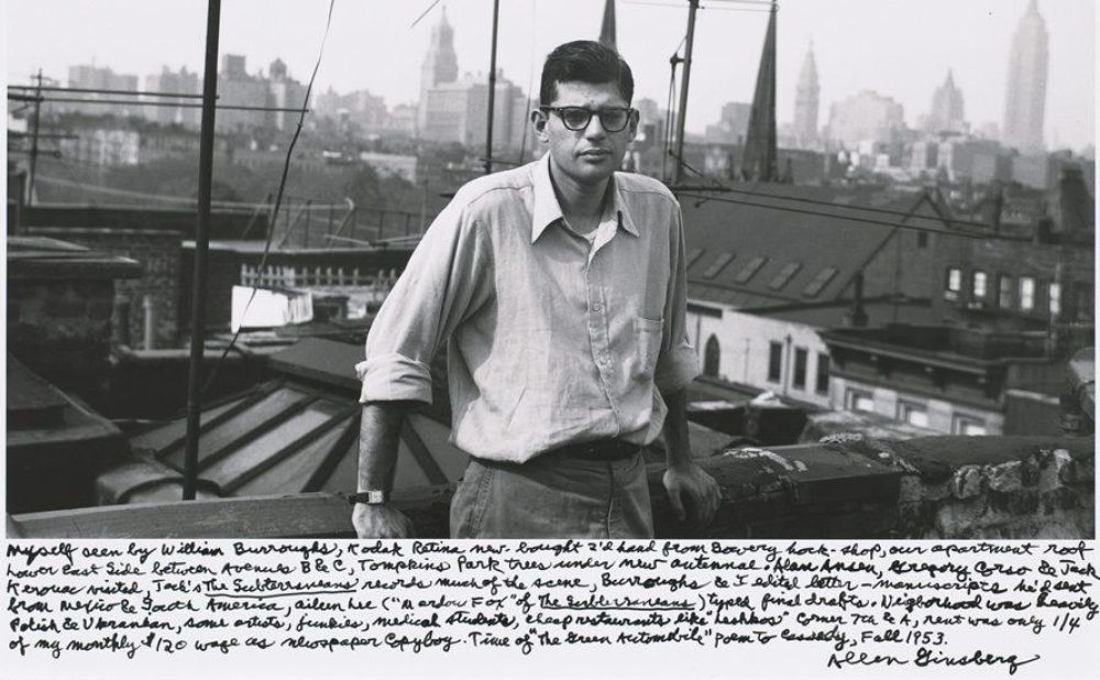 A man bespectacled man stands on a rooftop with a foggy cityscape in the background.  Transcribed Text:  Myself seen by William Burroughs, Kodak Retina new bought 2¼ lens from Bowery shop, our apartment roof lower East Side, retoken Avenue B El, Tompkins Park trees unseen, mist Autumnal dawn haze, Exaggerated to see the known writing. Joel's The Subterraneans records much of the scene, Burroughs to be still better Mannescripted his decision from Mexico to South America, Aimee seen in 'The Andes' etc, of the restless back. Typed final drafts, Negroes mud cakes, Polish & Ukranian, Aces edit, Fischer's, Michael’s theatre, cheap restaurants, the Hudson’s corner, Tan & JuR, hand over type 1/4 of my monthly 1/2 wage as newspaper copyboy. Time of the dawn interminable point to Cassidy, Fall 1953. Allen Ginsberg