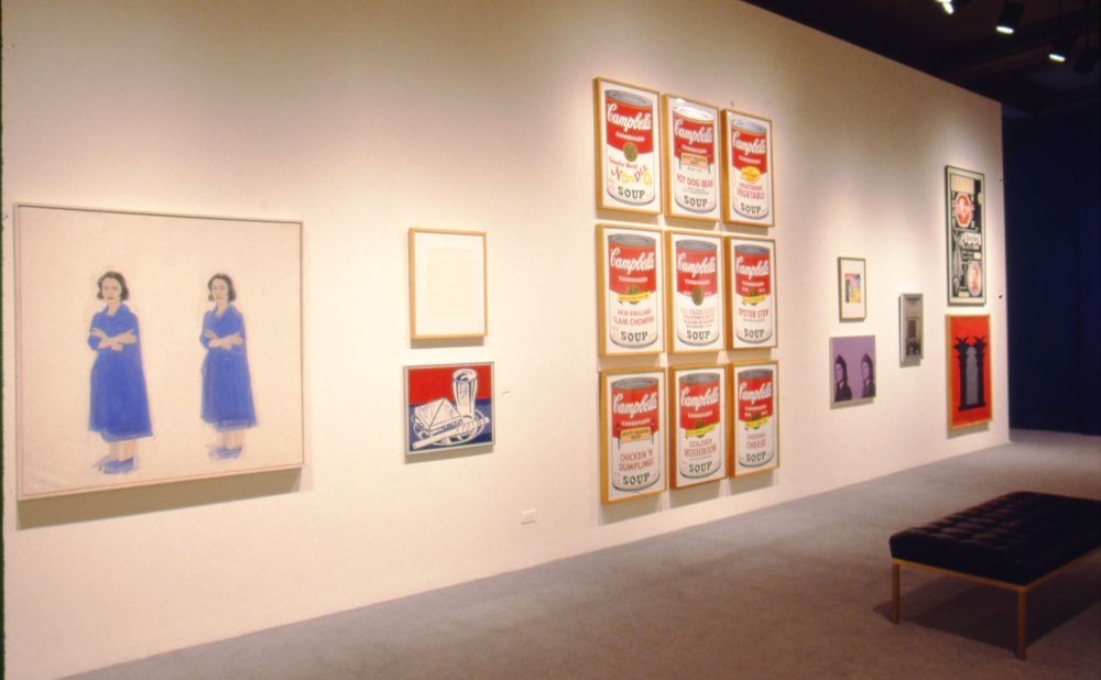 Art gallery with various artworks, including paintings of two figures, Campbell's Soup cans, and other framed pieces.
