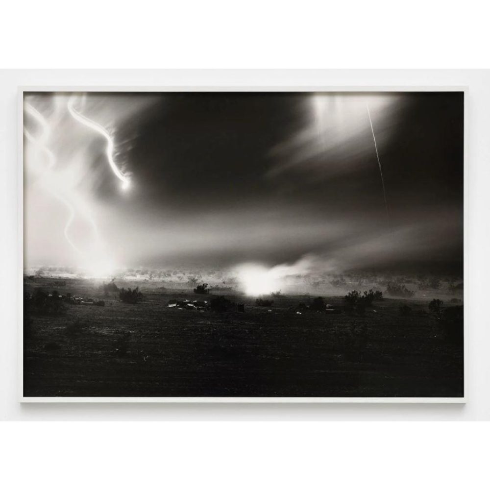 A black-and-white photograph in a thin white frame shows a vast nighttime, desert landscape on which military vehicles ride and conduct training
