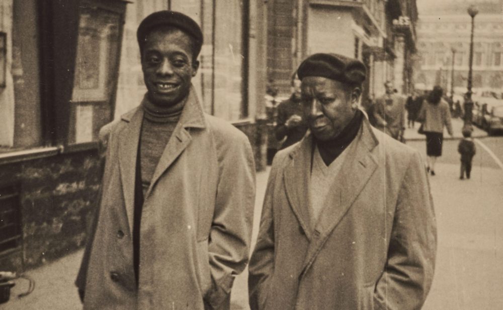 Two Black men in overcoats and hats walking down a city street