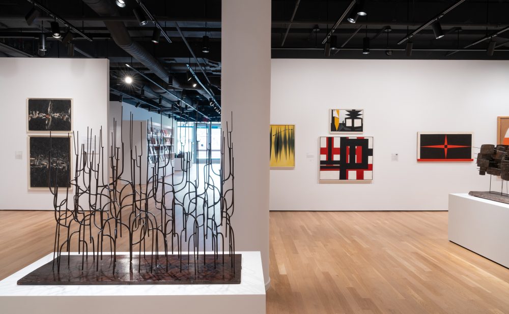 An art gallery with sculptures and abstract paintings on the walls and wooden flooring.