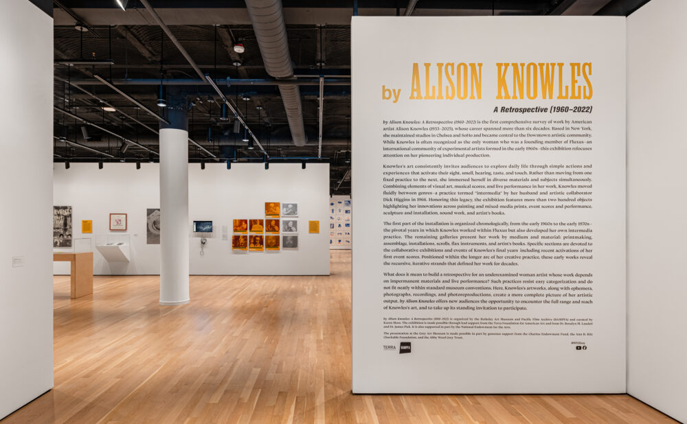 Museum gallery with artworks on white walls and a large introductory panel for “by Alison Knowles: A Retrospective (1960–2022).” Alt text generated by AI.