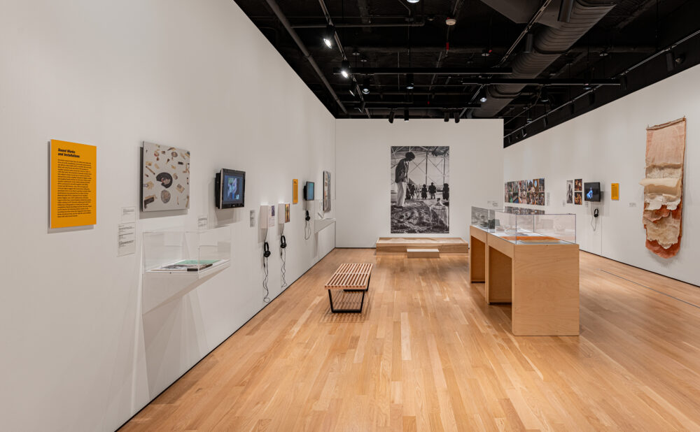 Interior of a contemporary art gallery displaying mixed-media artworks, photographs, videos, sculptures, and artifacts. Alt text generated by AI.