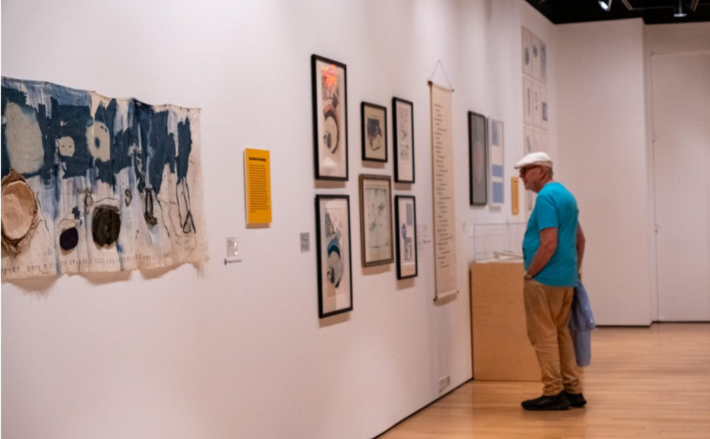Person viewing abstract artwork and framed pieces in a brightly lit gallery.