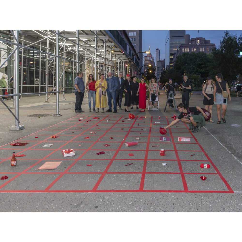 People gather beside a red-taped grid installation scattered with objects on a downtown sidewalk at dusk. Photo generated by AI.
