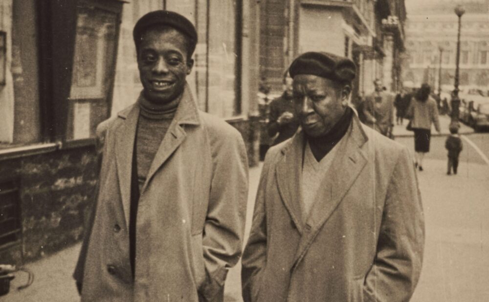 Two Black men in overcoats and hats walking down a city street