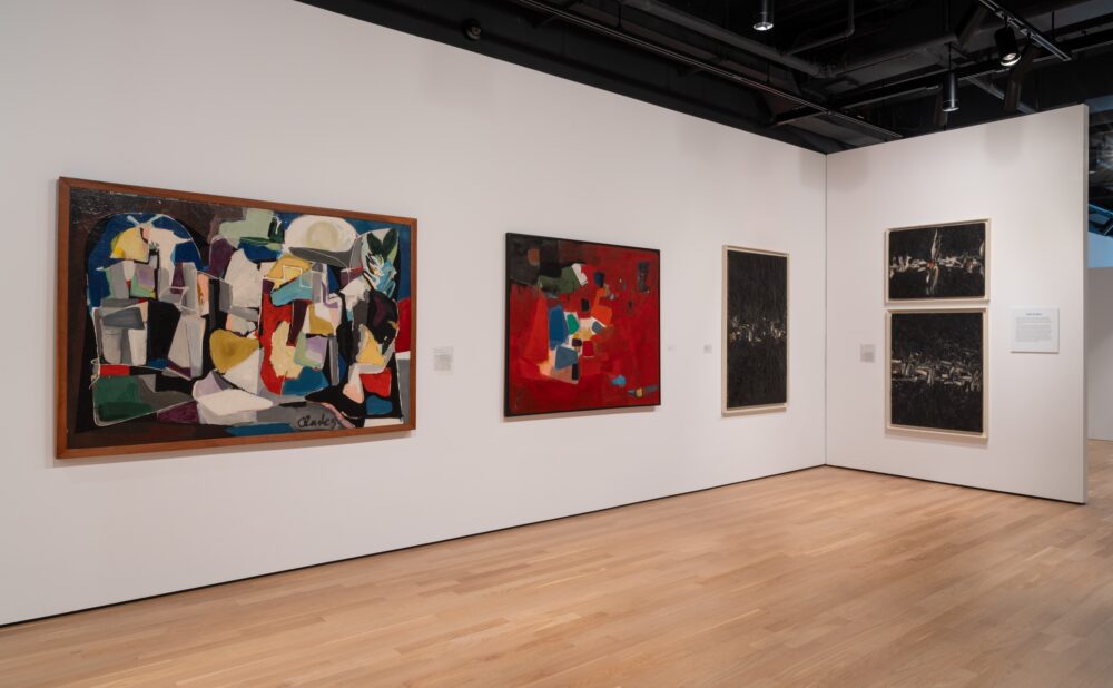 Abstract paintings in an art gallery with wooden floors and white walls.