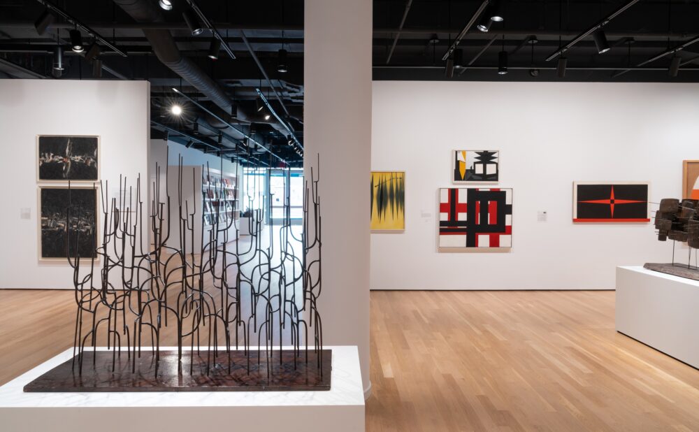 An art gallery with sculptures and abstract paintings on the walls and wooden flooring.