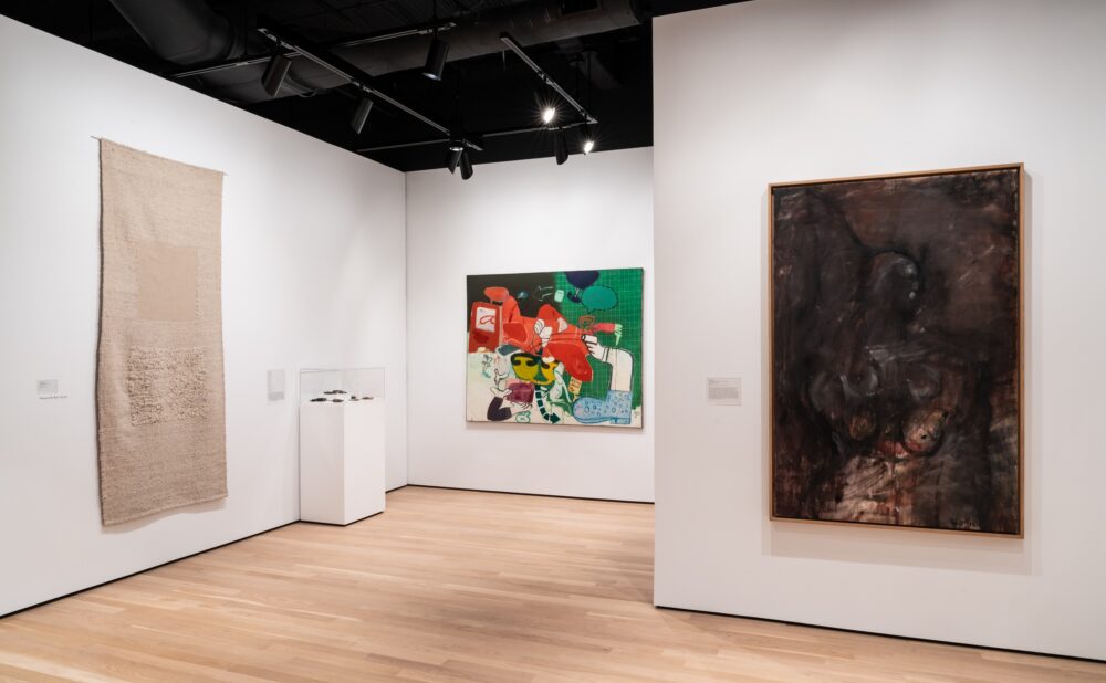 An art gallery showcasing textile art, a colorful abstract painting, and a dark-toned painting.