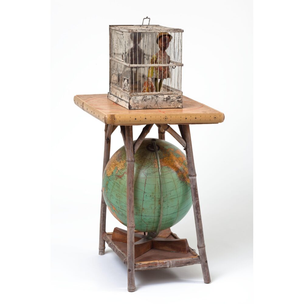 Assemblage comprised of a small table with a globe underneath, with a birdcage atop holding a vintage doll.