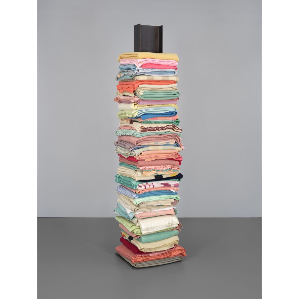 A colorful stack of blankets folded up and stacked atop each other on a steel i-beam, which acts as a sort of armature