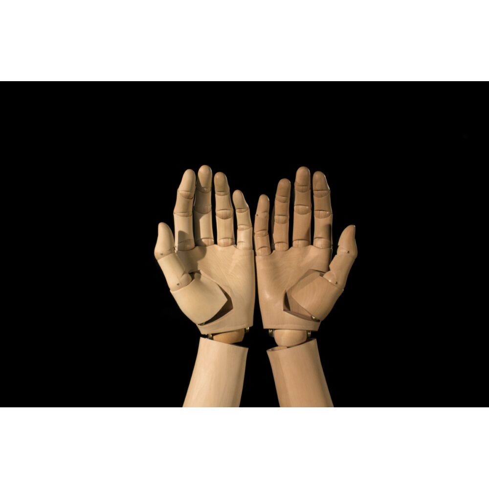 A pair of puppet wooden hands aside each other, palms up, facing the viewer, against a black screen