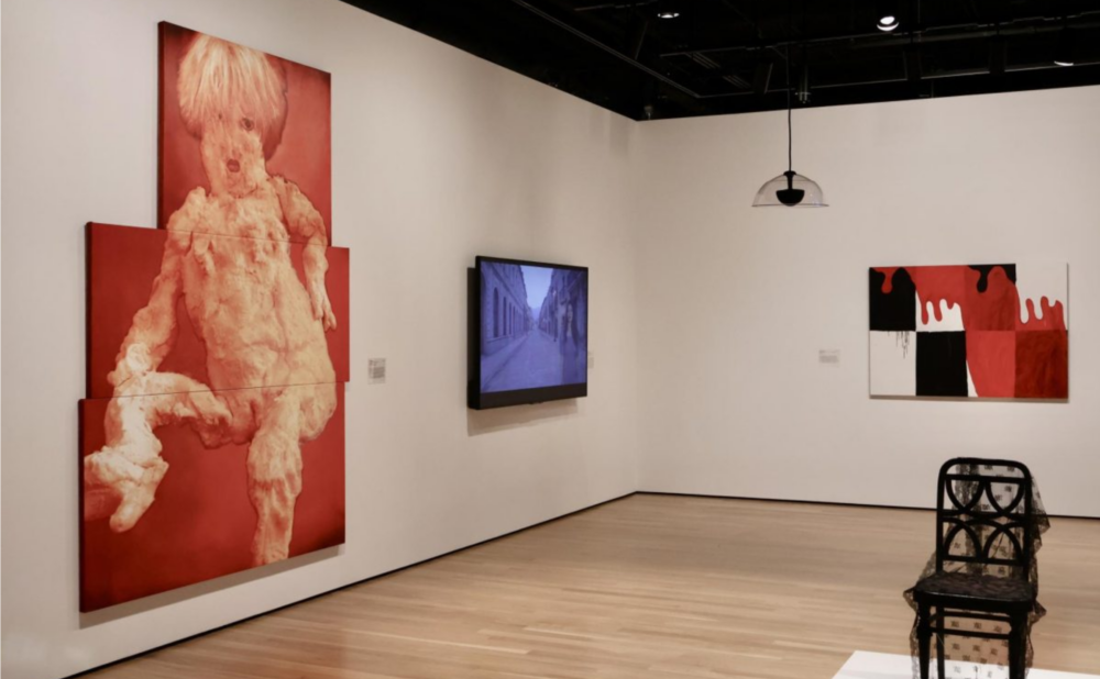 Mdoern art museum with abstract paintings, a video display, and a lace-covered chair on a pedestal.