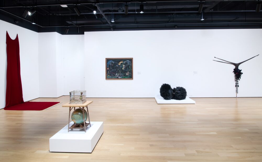 Modern art museum featuring a sculptures on platforms, textile sculptures on the wall, and a framed multimedia artwork.