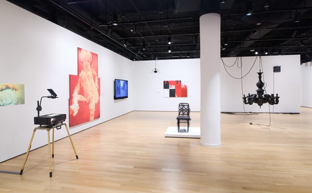Modern art museum with various sculptures and paintings on display against white walls and wood flooring.