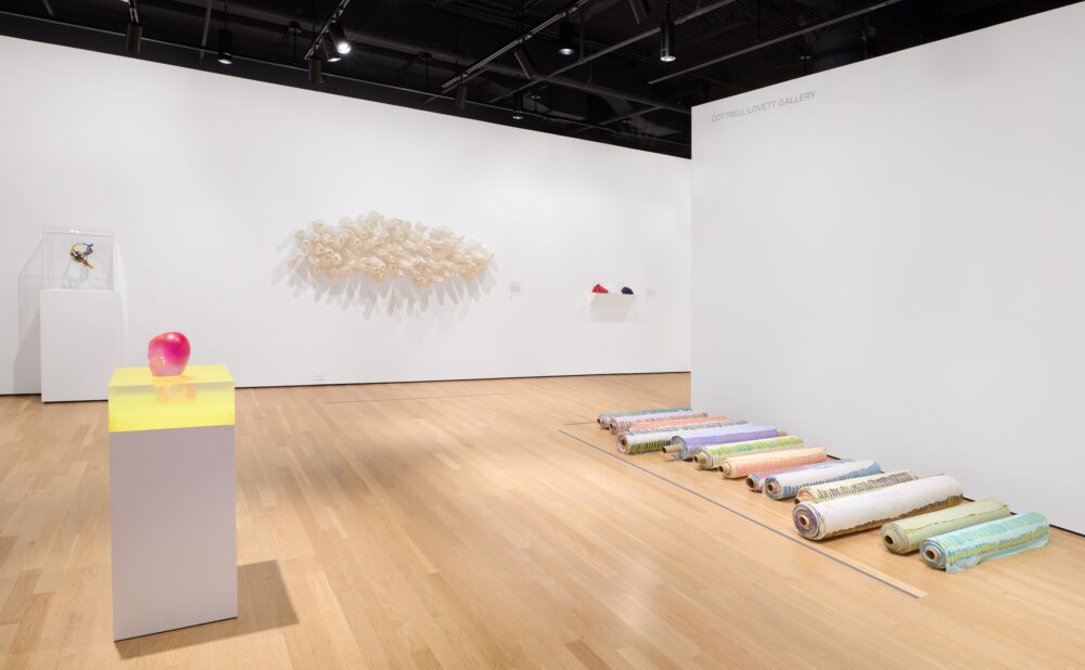 Modern art museum with various sculptures and paintings on display against white walls and wood flooring.