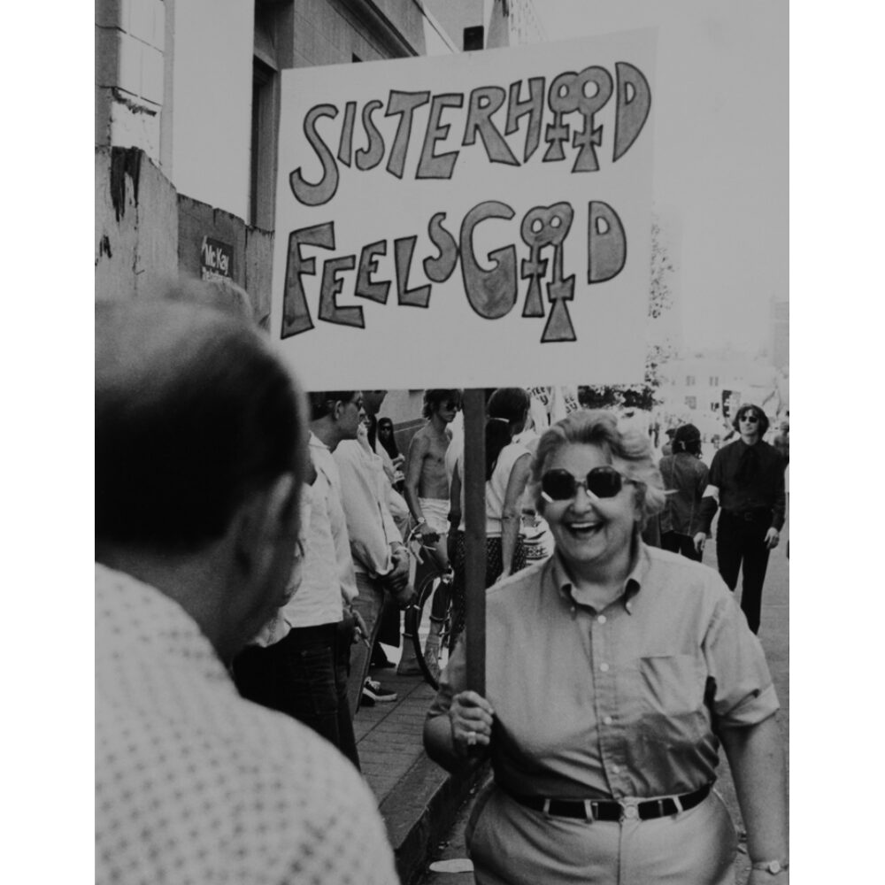 Black-and-white photograph of activists gathered outdoors near protest signs. (Alt-text generated by AI)