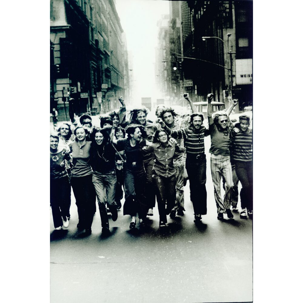 Black-and-white photograph showing a group of people marching down a city street together. (Alt-text generated by AI)
