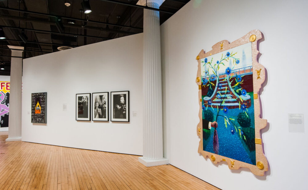 Gallery displaying multiple framed artworks, including a large colorful framed piece on the right wall. (Alt-text generated by AI)