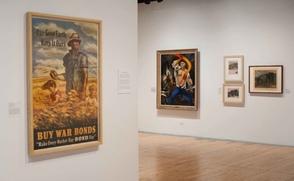 Gallery wall section highlighting a framed World War II propaganda poster on the left and framed paintings on the right. (Alt-text generated by AI)