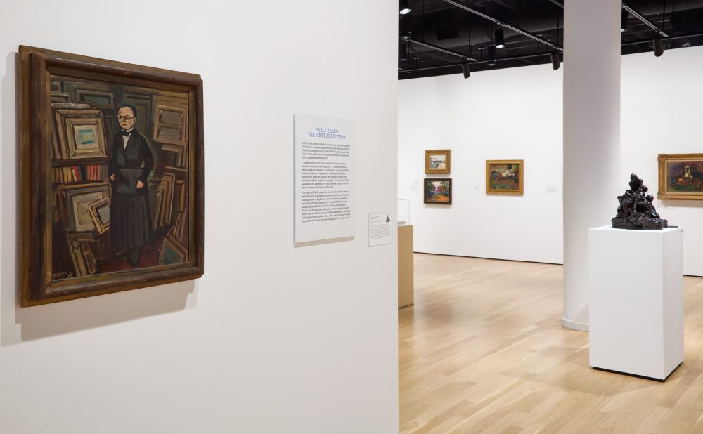 Art gallery with paintings and a text panel on the walls and a sculpture on a pedestal.