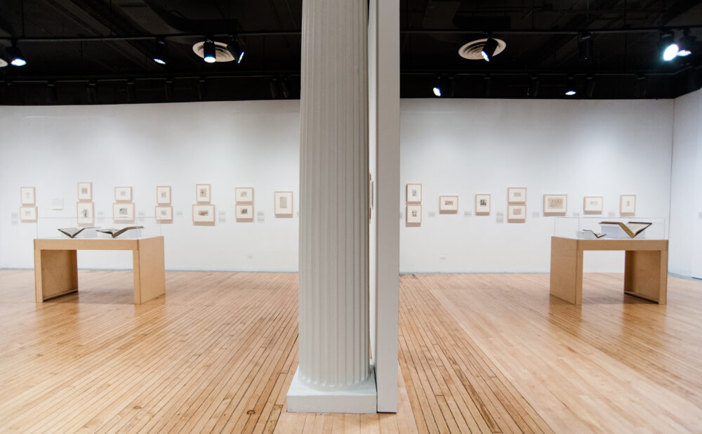 Open exhibition hall featuring a central white pillar and multiple wooden display cases positioned across the room. (Alt-text generated by AI)