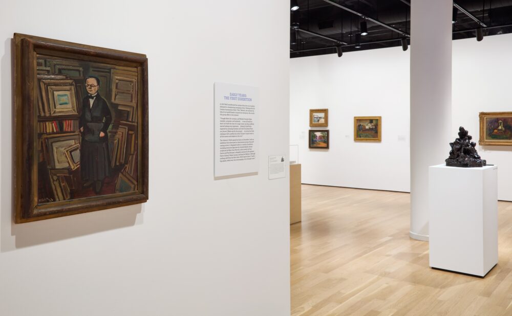 Art gallery with paintings and a text panel on the walls and a sculpture on a pedestal.