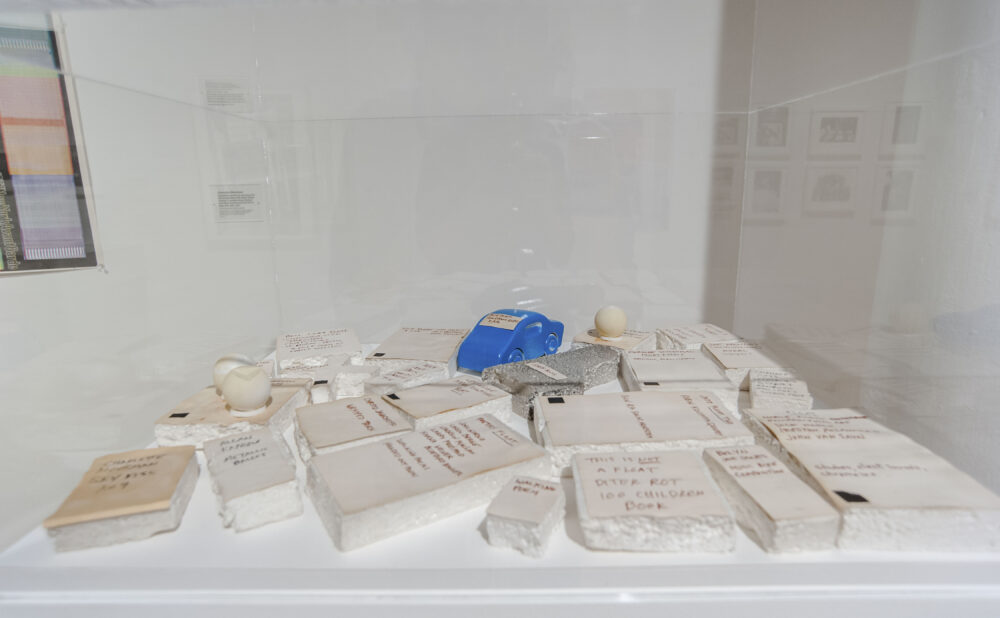 Close-up view of a large, low display table filled with plaster casts, books, and archival artifacts. (Alt-text generated by AI)