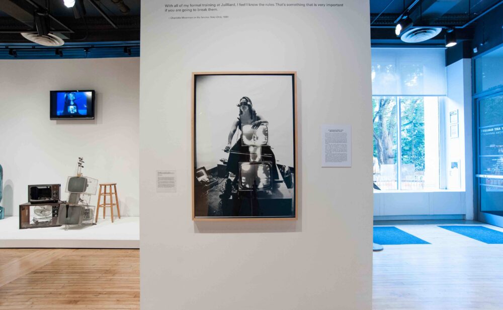 Gallery wall displaying a large framed performance photograph beside a doorway with windows facing the outdoors. (Alt-text generated by AI)