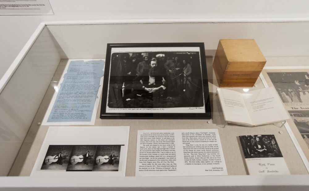 Overhead view of a vitrine containing historical performance documentation, open books, and archival photos. (Alt-text generated by AI)