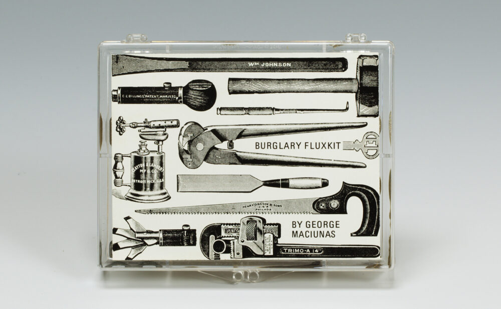Transparent plastic case displaying a black-and-white collage of hand tools labeled “BURGLARY FLUXKIT” and “BY GEORGE MACIUNAS.” Alt text generated by AI.