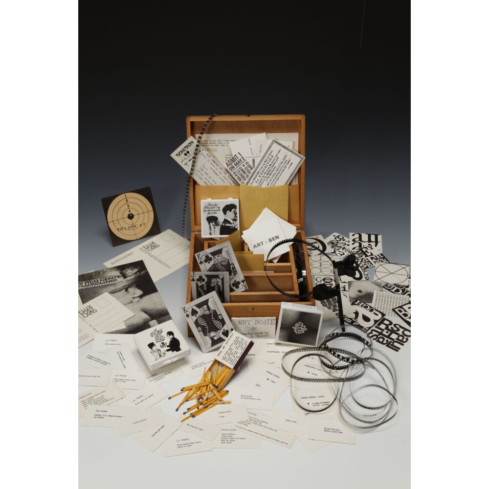 An open wooden box filled with printed cards, papers, and small objects on a table surface. Alt text generated by AI.