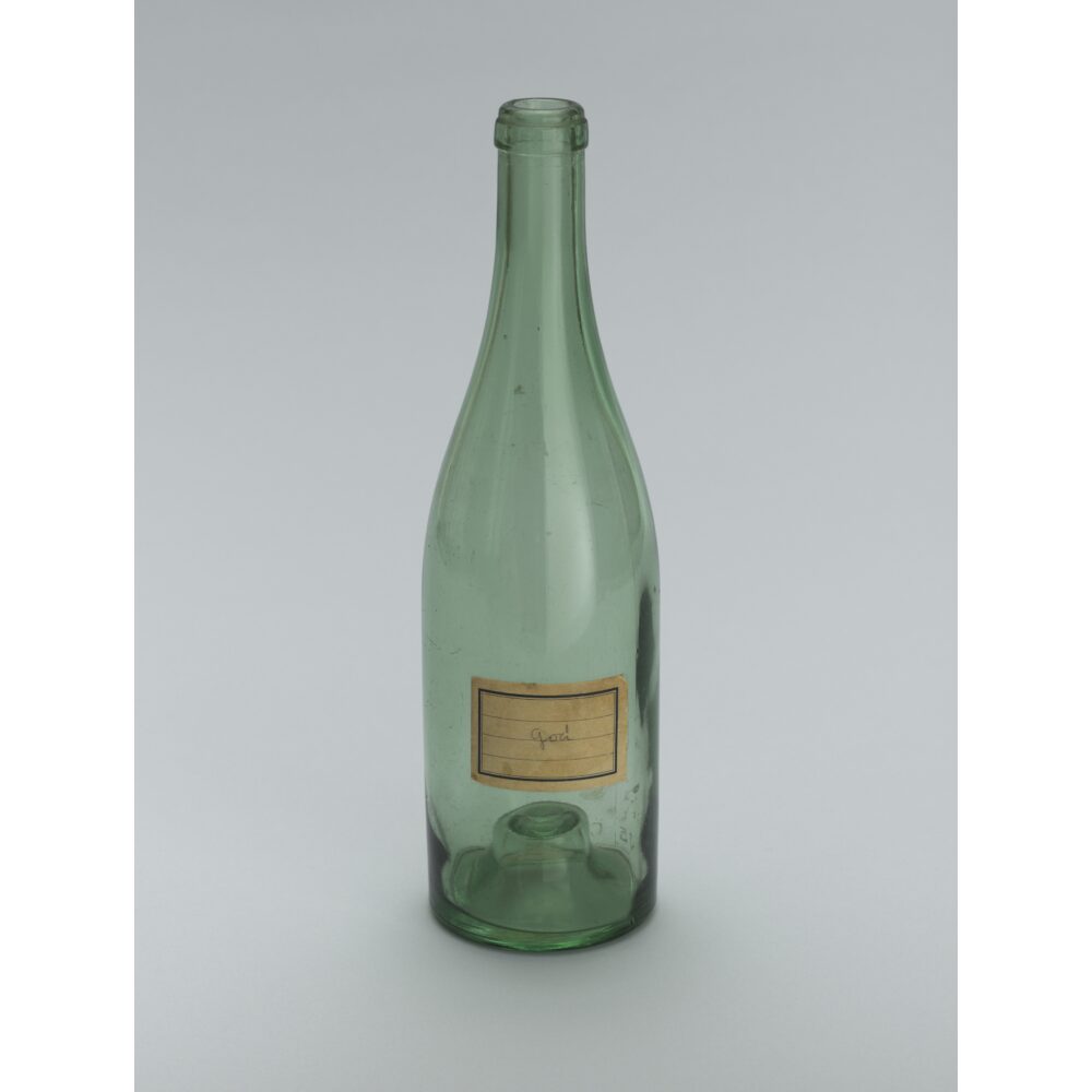 A green glass bottle with a label sitting upright on a light surface. Alt text generated by AI.