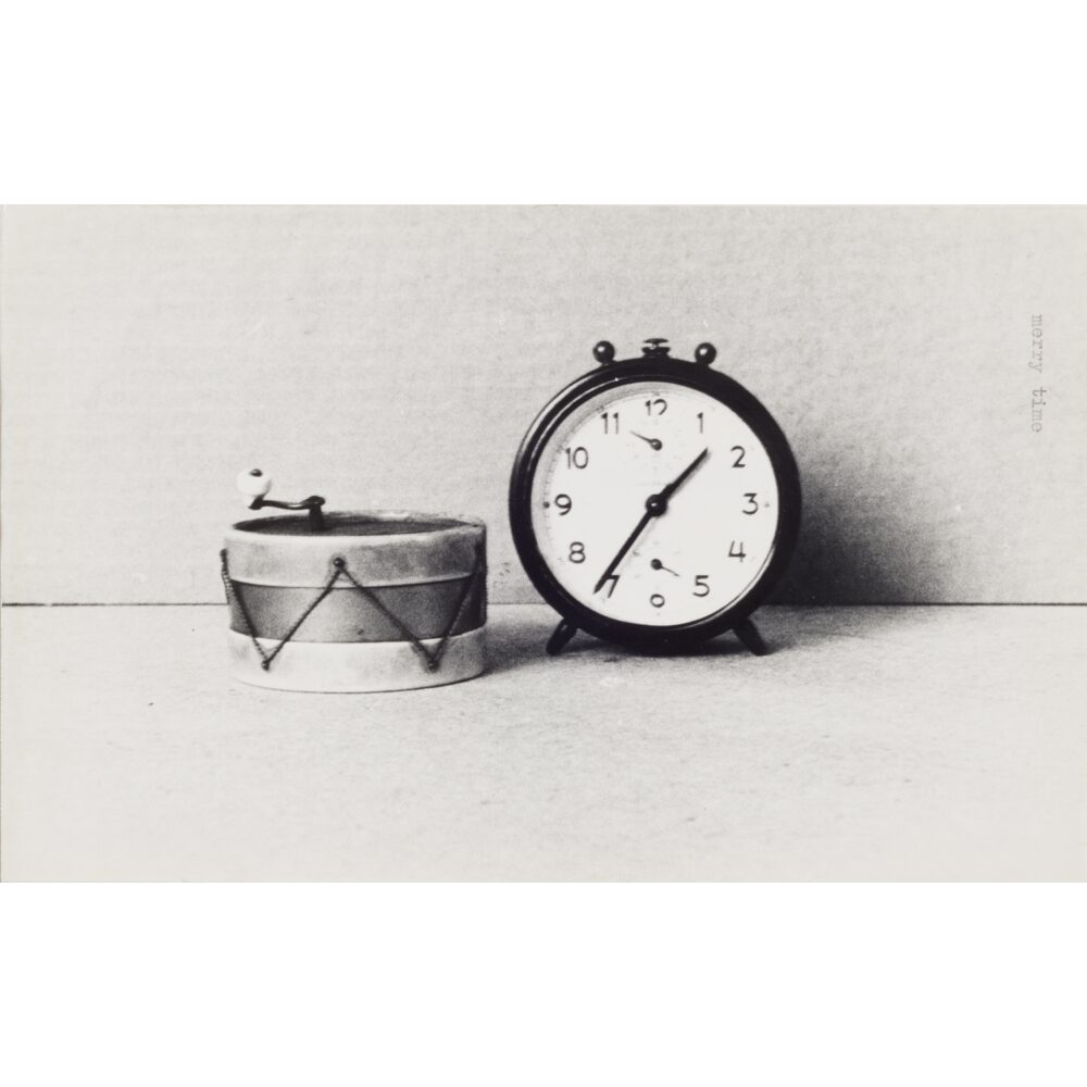 A black-and-white image of a small round alarm clock next to a cylindrical container. Alt text generated by AI.