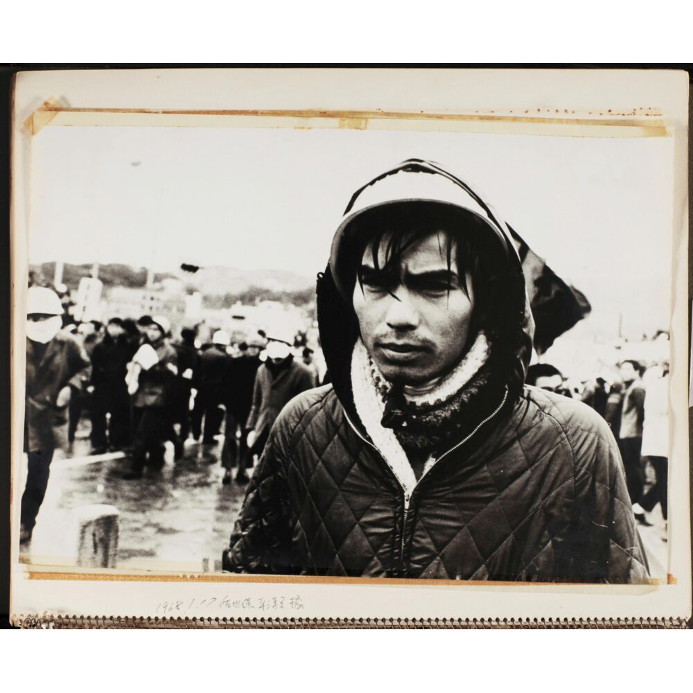 Black-and-white portrait photograph of a young man wearing a hooded jacket looking toward the camera by Shunji Dodo. (Alt-text generated by AI)
