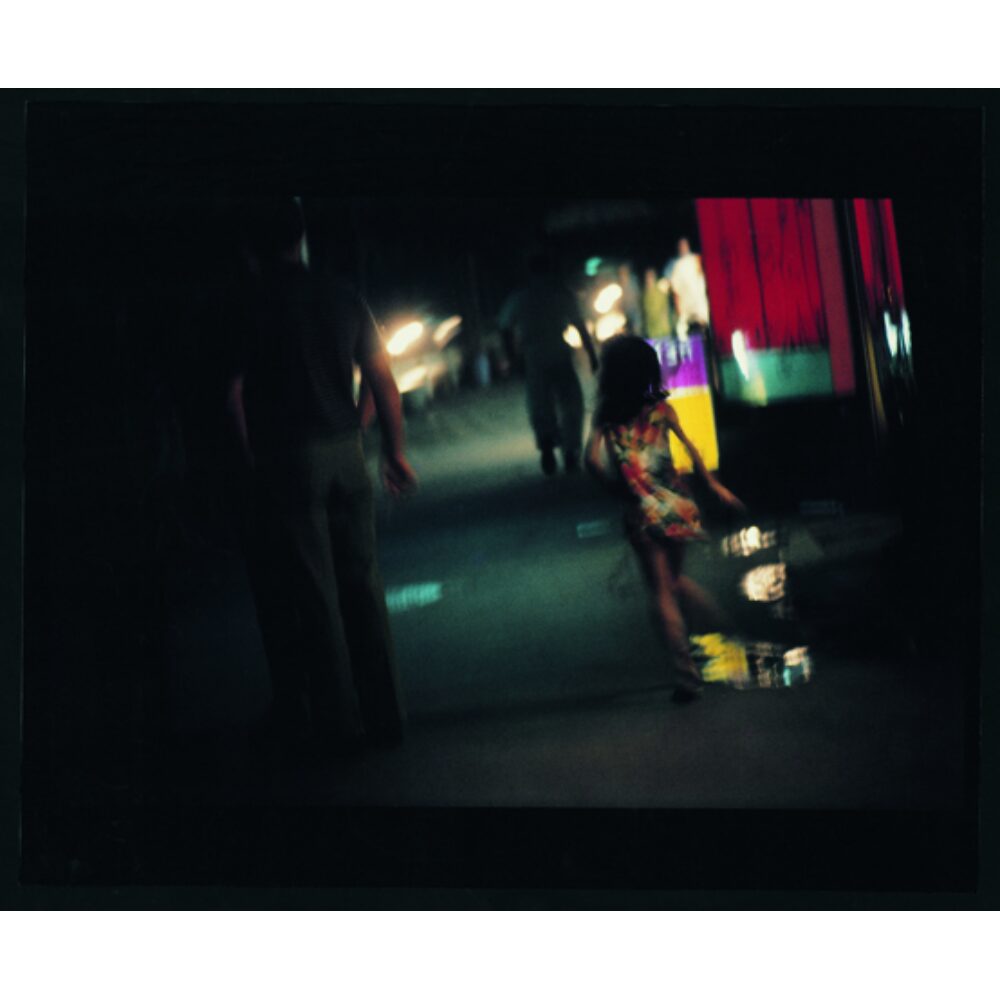 Dark, grain-heavy color photograph of a night scene in Yokosuka by Daido Moriyama. (Alt-text generated by AI)
