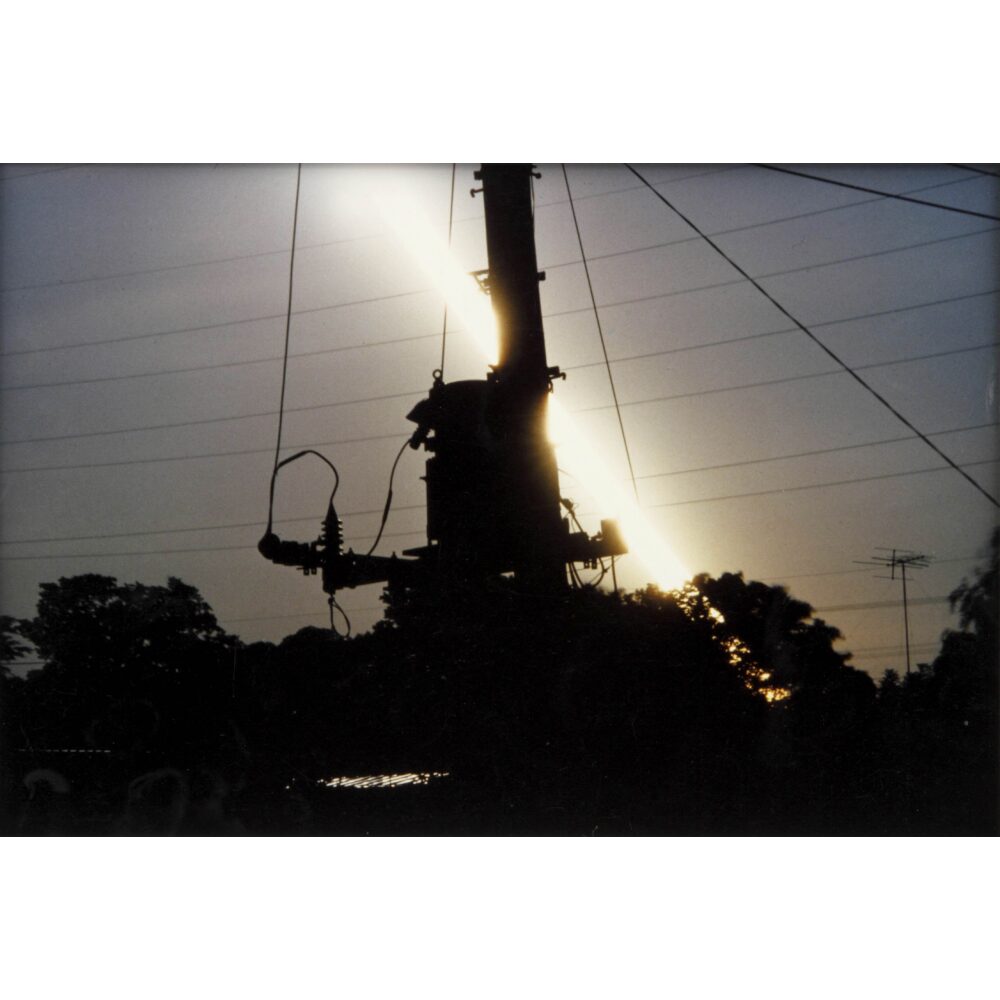 igh-contrast photograph showing a silhouette of an industrial structure against a bright horizon by Hiroshi Yamazaki. (Alt-text generated by AI)