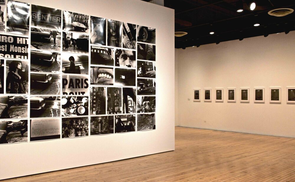 Large-scale wall grid composite of high-contrast black-and-white photographs facing an adjacent wall hung with a horizontal photo series. (Alt-text generated by AI)