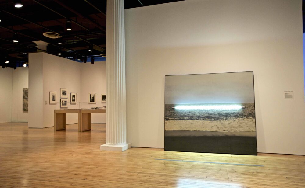 Wall-mounted artwork featuring a glowing horizontal tube light installed over an ocean landscape photograph. (Alt-text generated by AI)