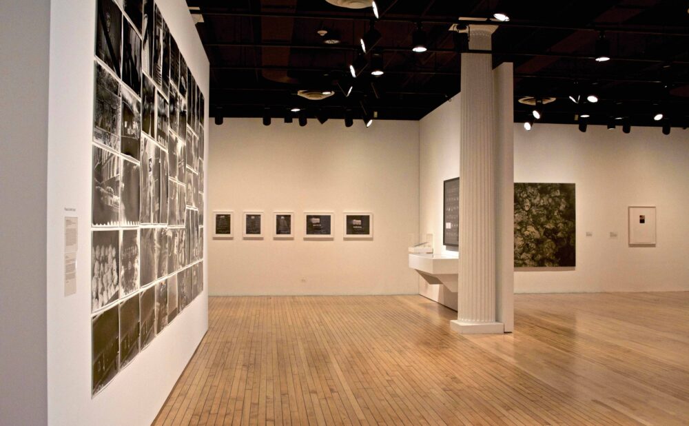 Perspective view showing a large photo-grid wall on the left leading into a bright exhibition hall with architectural columns. (Alt-text generated by AI)