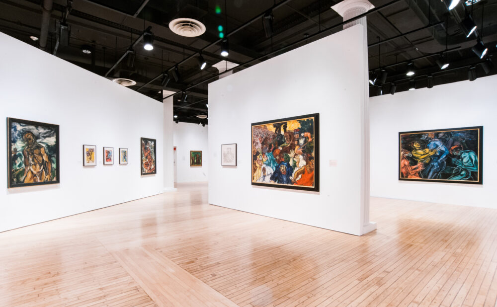 Angle shot looking down a gallery partition corridor lined with small-to-medium framed paintings. (Alt-text generated by AI)
