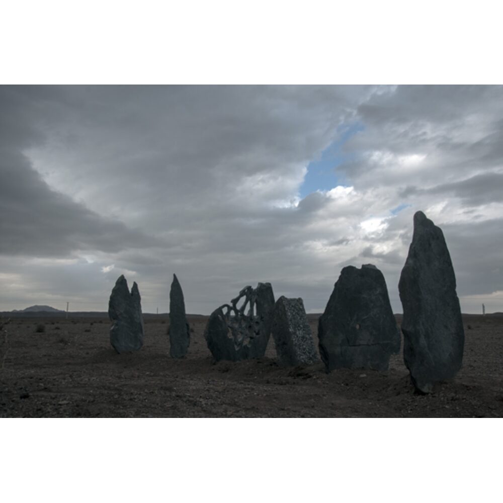 Atmospheric landscape photograph showing standing megalithic stone monuments under a dramatic cloudy sky by Barbad Golshiri. (Alt-text generated by AI)