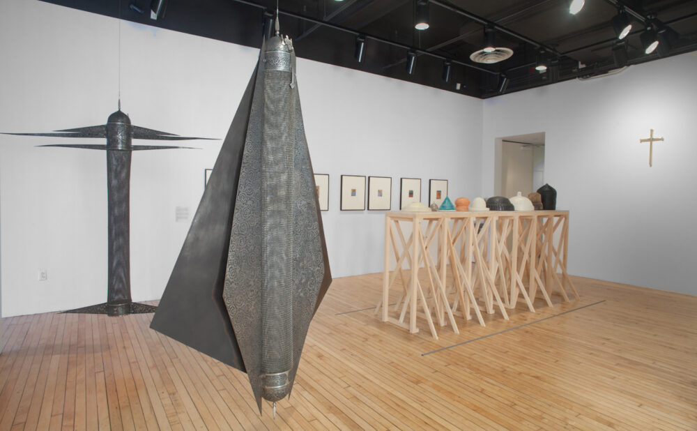 View of large-scale, dark geometric sculptures and a wooden frame installation positioned on polished hardwood flooring. (Alt-text generated by AI)