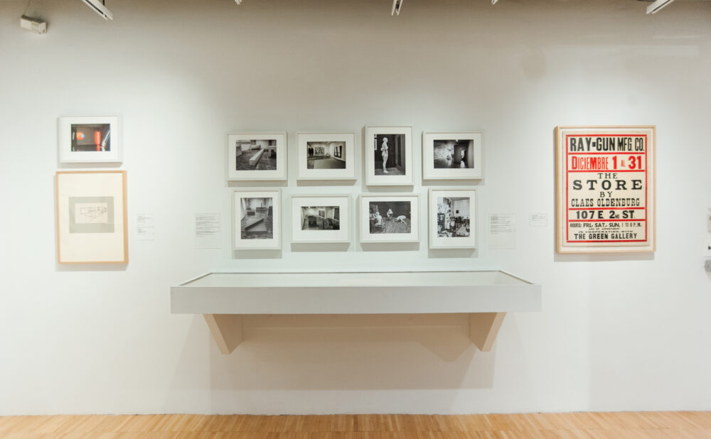 Gallery wall section with small black-and-white photos arranged above a white ledge and a red poster on the right. (Alt-text generated by AI)