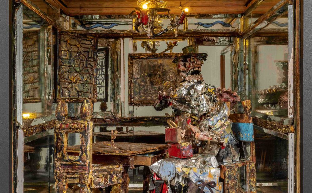 A diorama of a dining room with a figure made of reflective scraps seated at a table, surrounded by mirrors.