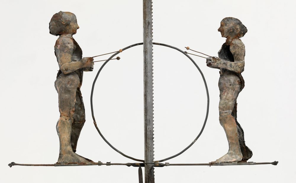 Metal sculpture of two facing figures with rods, separated by a vertical saw blade.