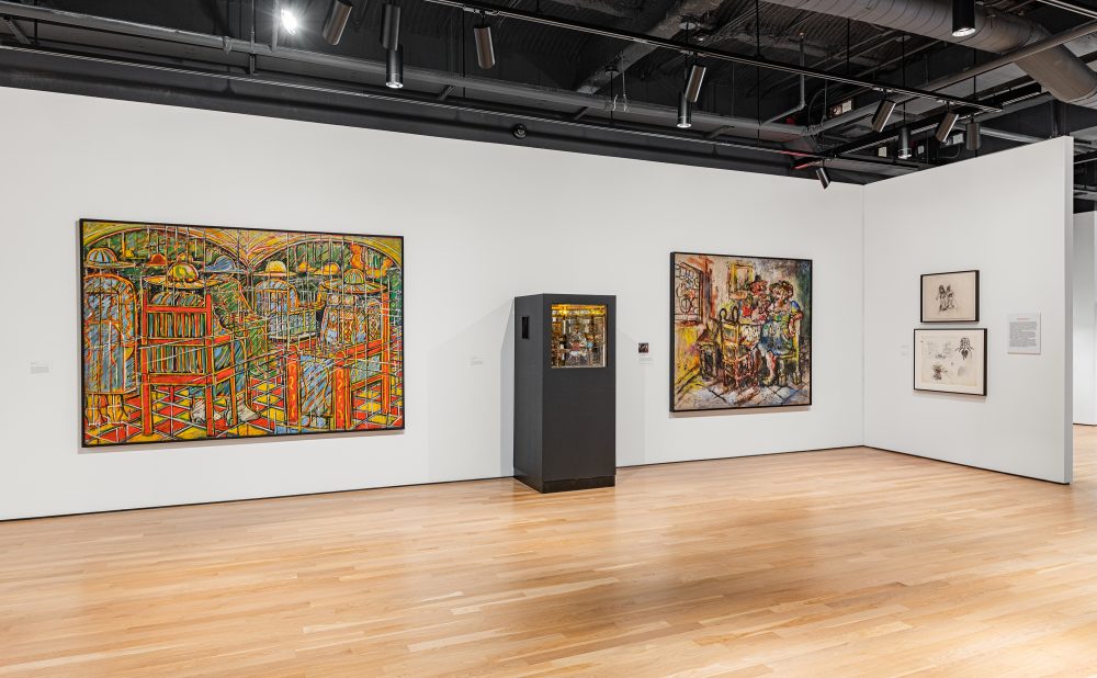 Art gallery with colorful abstract paintings and drawings, and a tall black display case containing an artful diarama, on a wooden floor.
