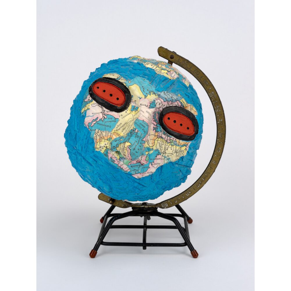 culptural artwork featuring a world globe modified with painted red-rimmed eye sockets on a dark display stand. (Alt-text generated by AI)