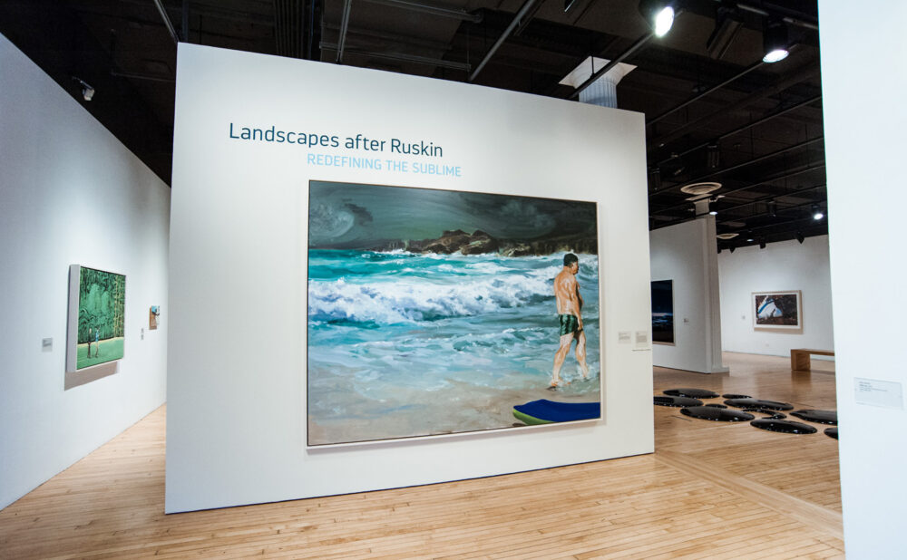 Central gallery entrance wall featuring a large, vibrant ocean landscape painting and exhibition title reading "Landscapes are Ruskin: Redefining the Sublime" (Alt-text generated by AI)